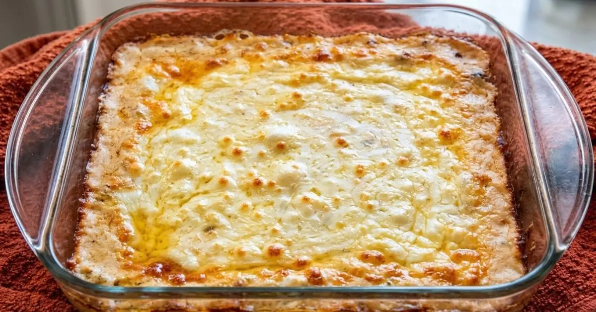 Hot, cheesy Steak-umm Philly cheesesteak dip fresh from the oven in a glass baking dish on a rust-orange kitchen towel.